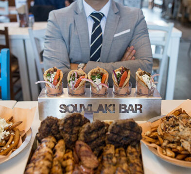 Suited person behind a rack of Souvlaki