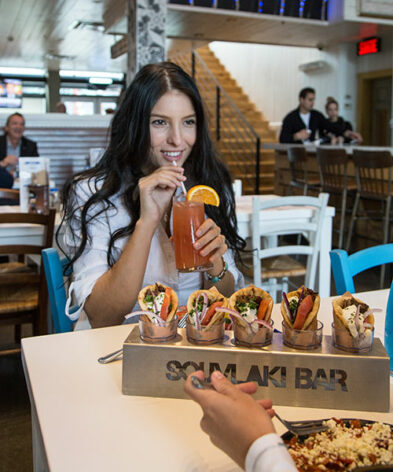 A brunette taking a sip of her Souvlaki Bar orange drink
